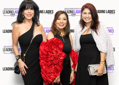 Three women smiling in front of logo step and repeat.
