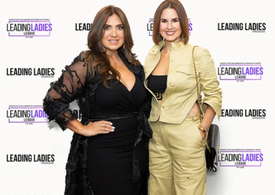 Two women smiling in front of logo step and repeat.