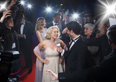 Beautiful woman on red carpet surrounded by interviewers and paparazzi.