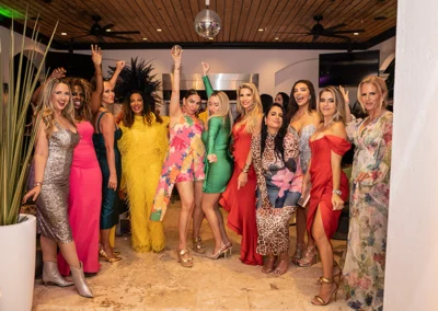 Group of women cheering and celebrating wearing colorful evening dresses.