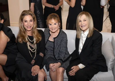 Three women dressed elegantly sitting on couch.