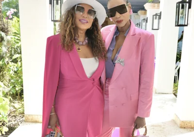 Two women in pink suits posing outdoors, one wearing a hat and sunglasses.