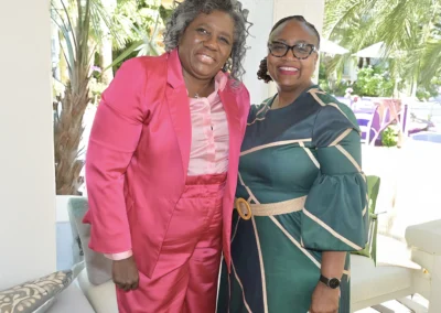 Two women smiling, one in a pink suit, the other in a green dress.